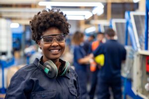 Smiling woman in safety glasses and headphones in a factory.