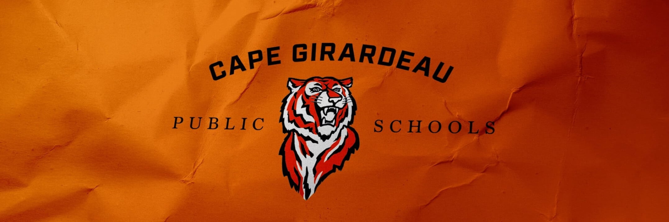 Cape Girardeau Public Schools logo featuring a roaring tiger mascot on orange crumpled paper background