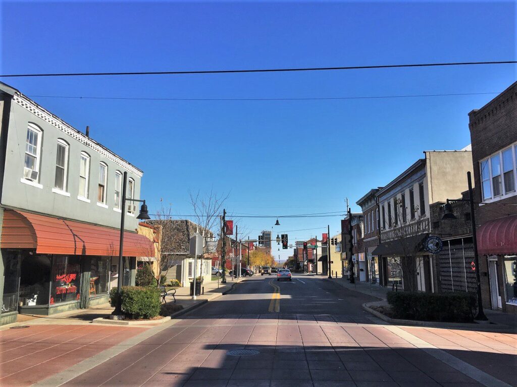 Sunny day on a quiet main street in a historic small town, with brick storefronts and clear blue sky.