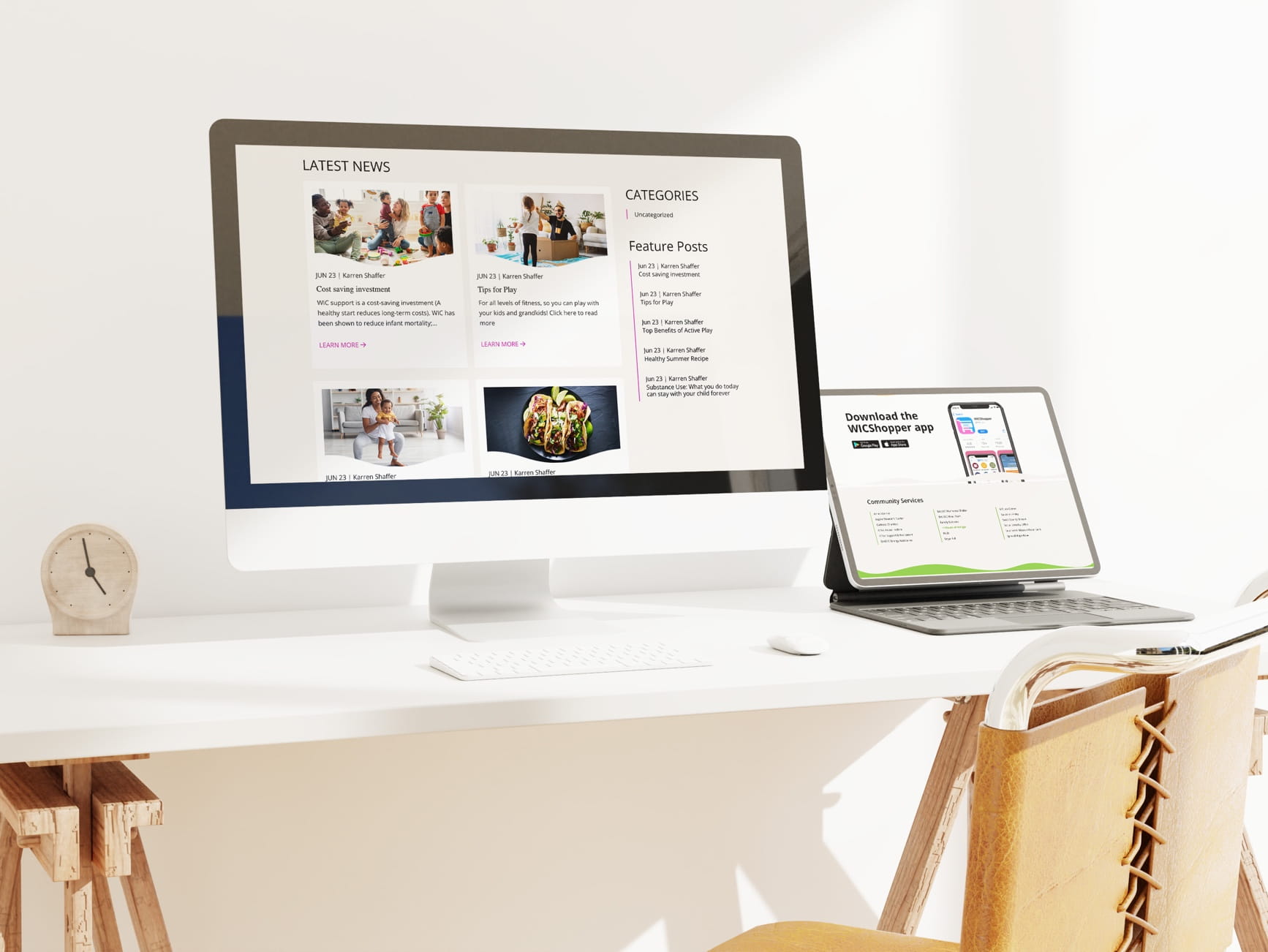 White desk with large monitor showing news site, tablet with app download, keyboard, mouse, wooden clock, and chair.