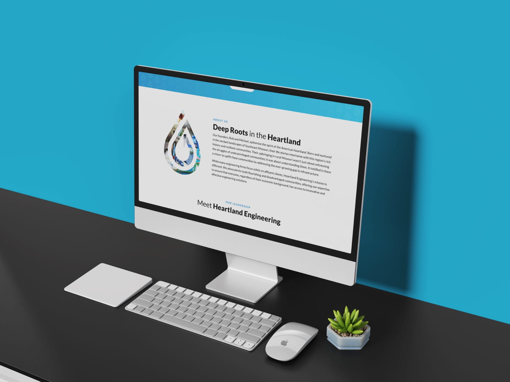 iMac showing Heartland Engineering 'About Us' page with Deep Roots in the Heartland logo, keyboard, mouse, succulent.