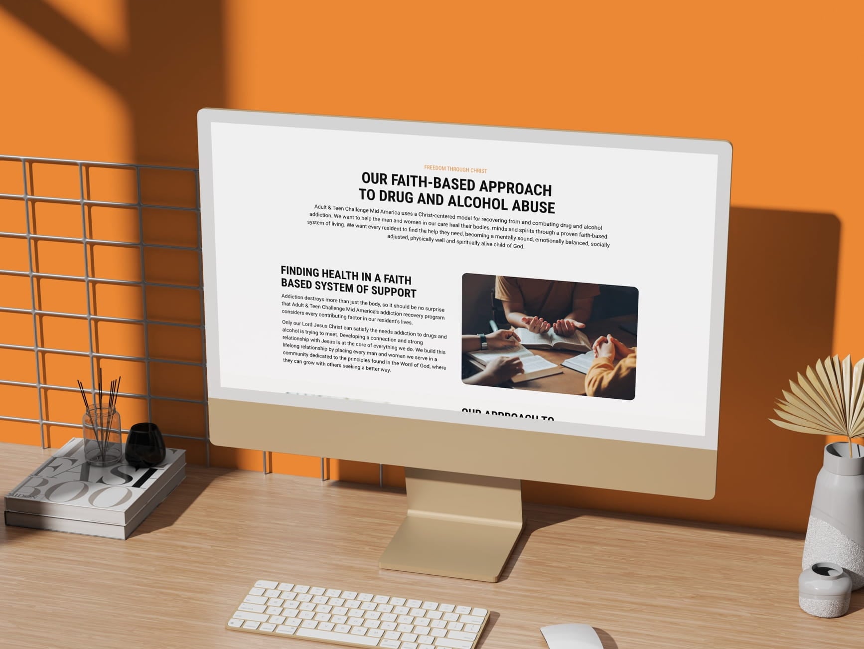 Monitor showing Adult & Teen Challenge Mid America's faith-based drug and alcohol recovery page on desk with orange wall.