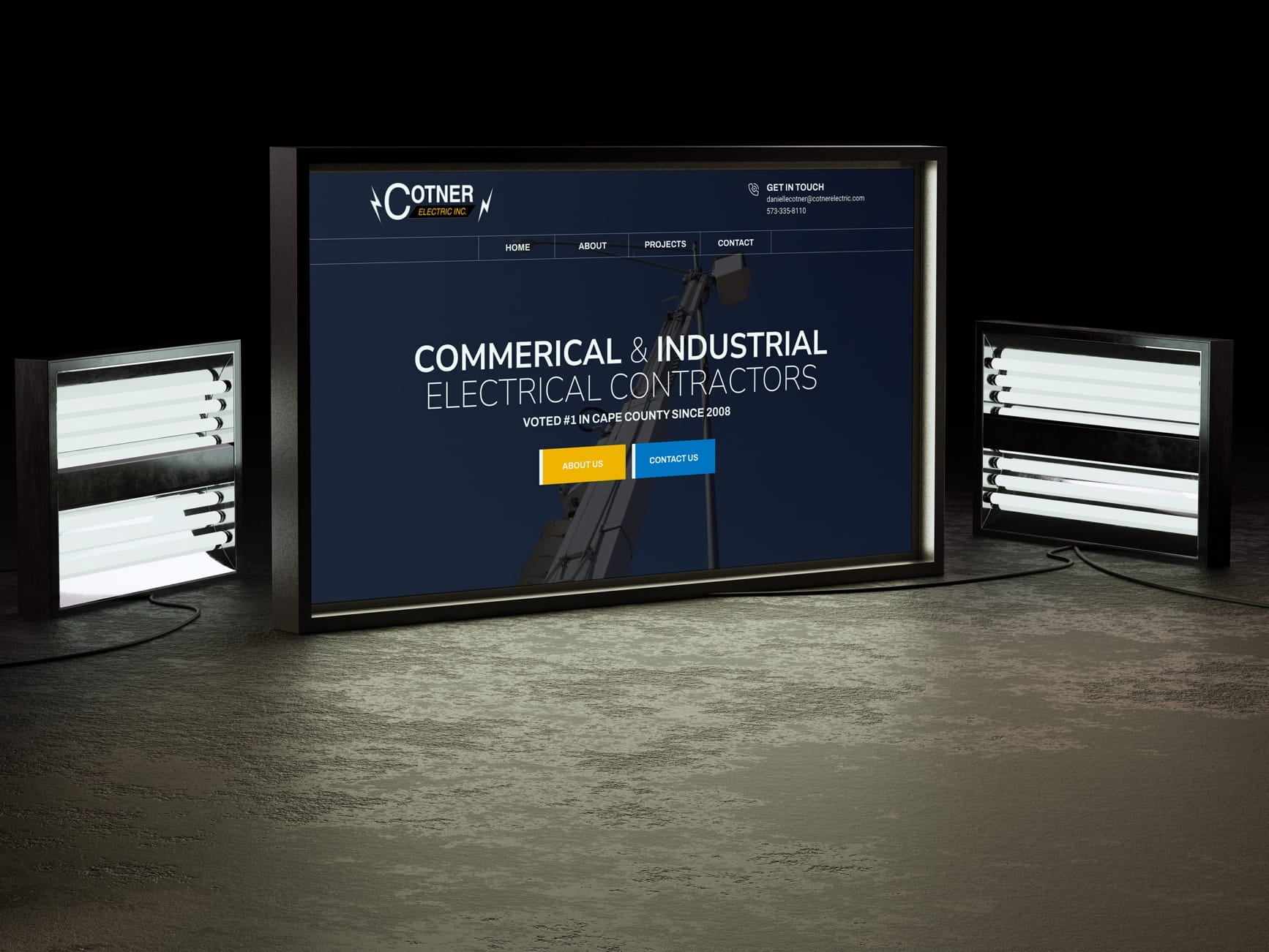 Screen displays Cotner Electric Inc. website for industrial electrical contractors, flanked by two light fixtures.