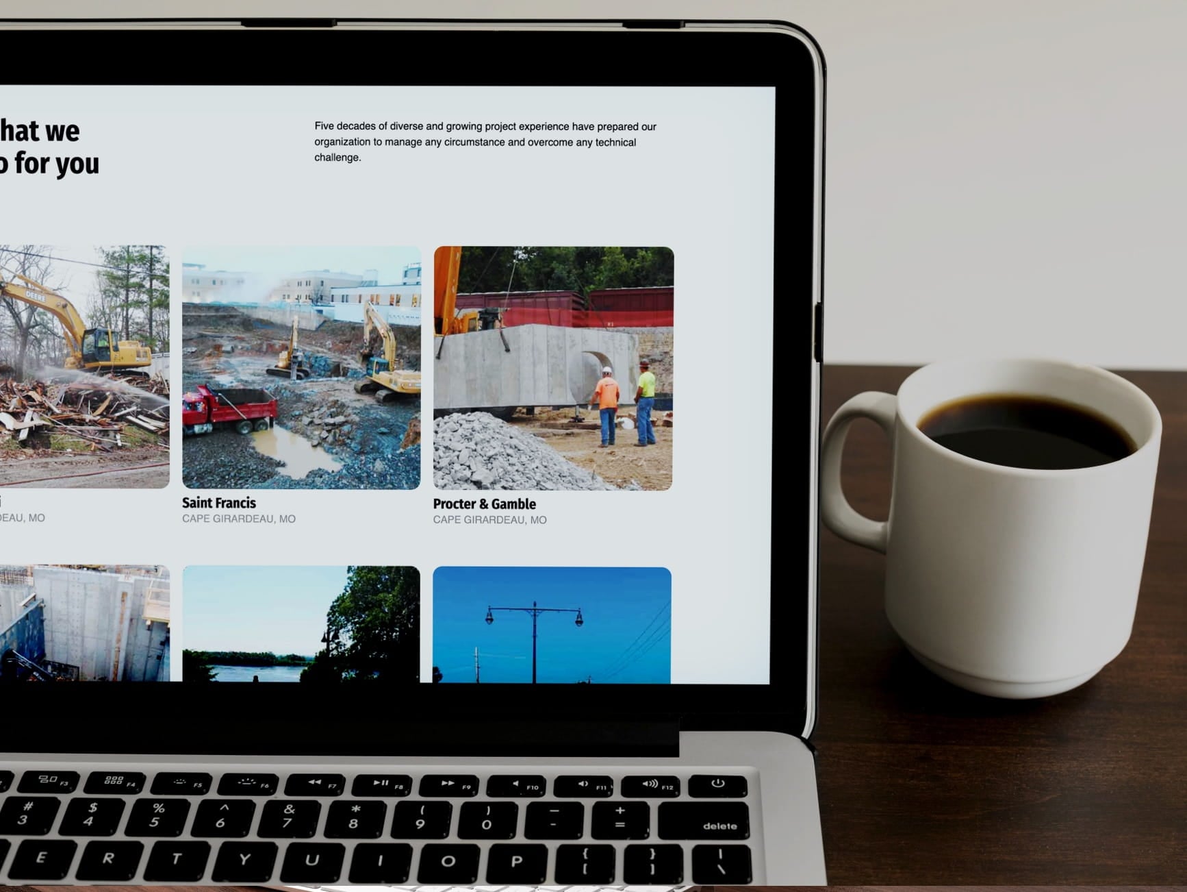 Laptop showing construction project portfolio photos beside a white coffee mug on a desk.