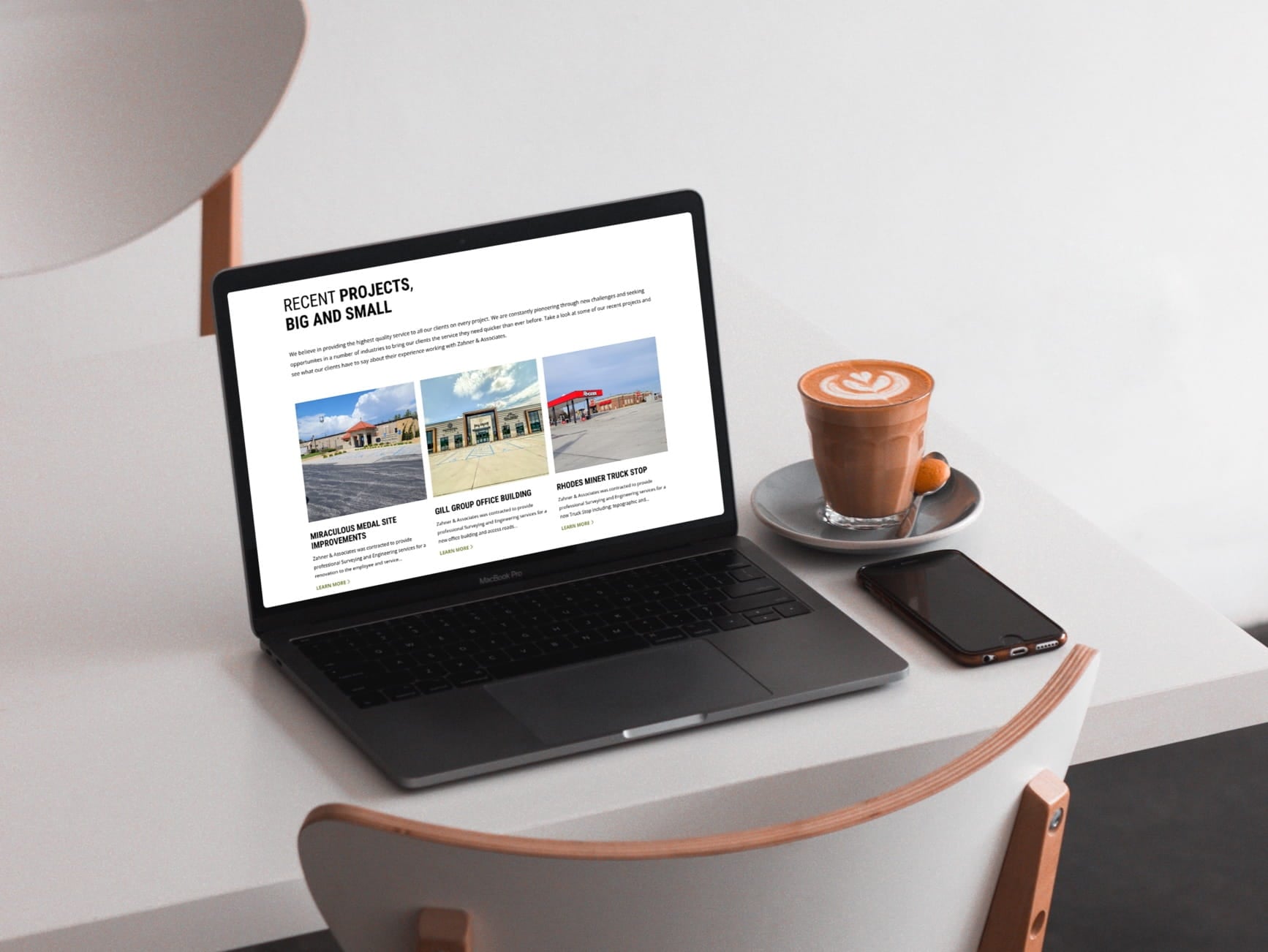 A laptop displaying a website with recent projects, next to a coffee cup, smartphone, and a modern chair.