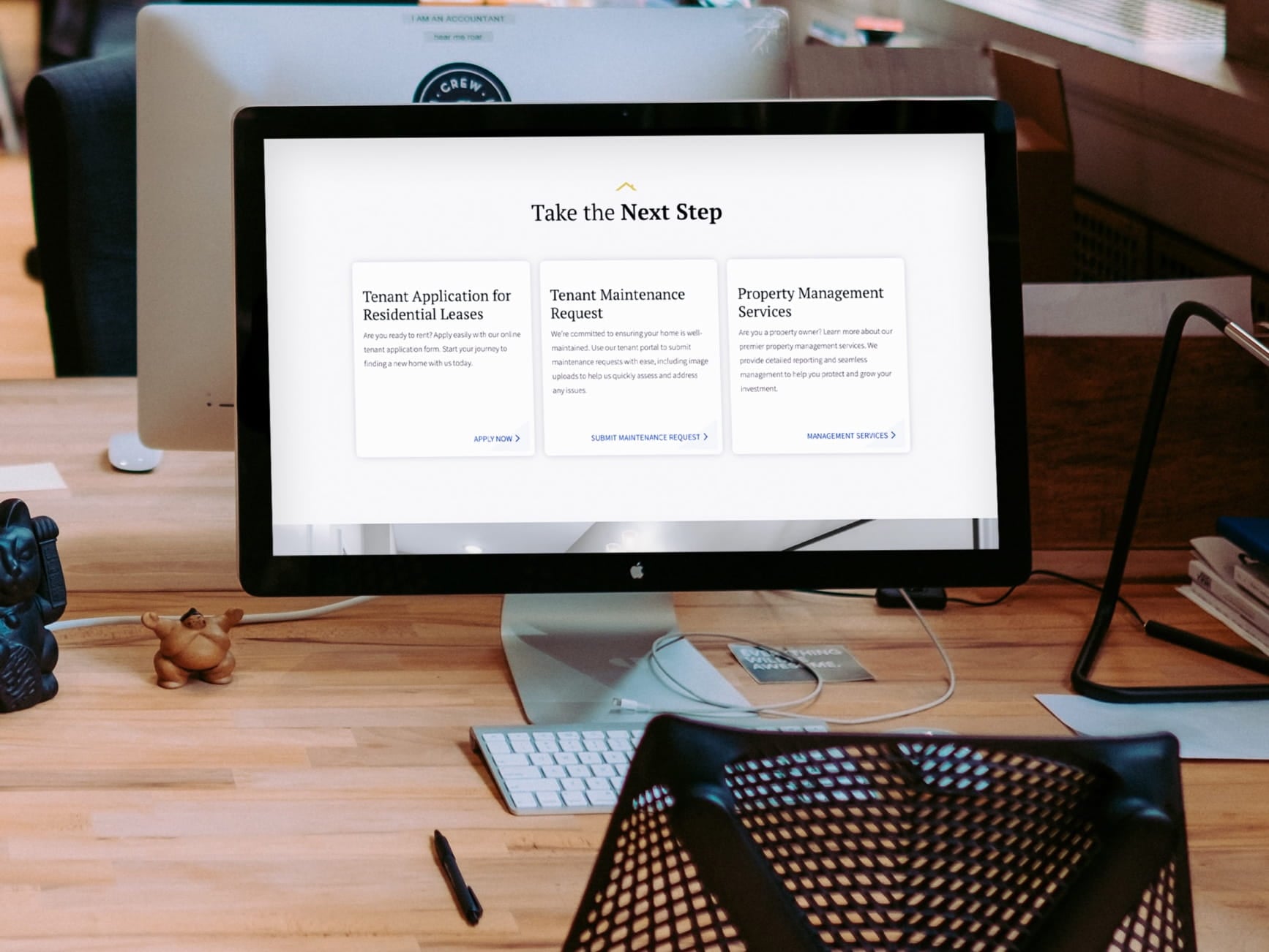 Monitor on desk shows real estate portal with tenant application, maintenance request, and property management options.