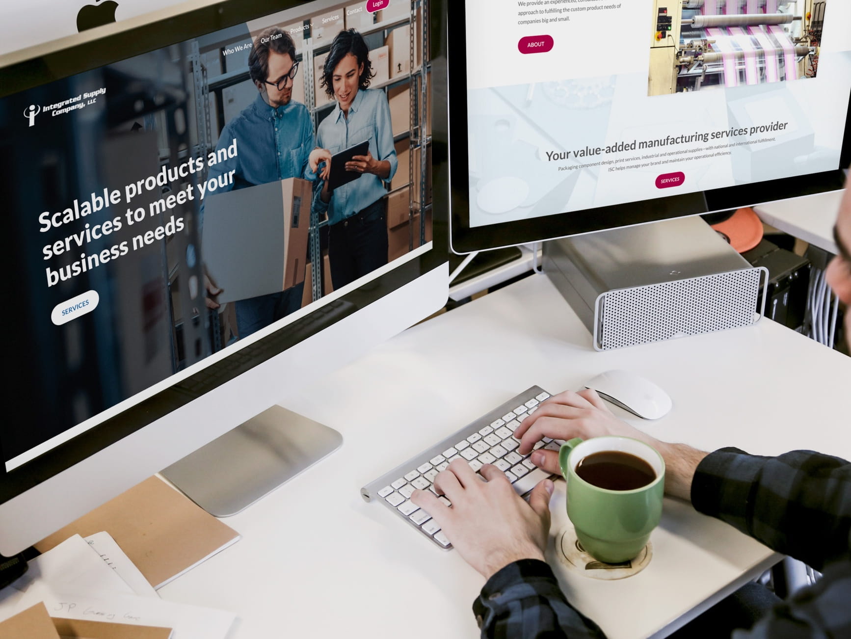 Person typing on keyboard at a white desk with dual monitors showing Integrated Supply Company website, coffee cup nearby.