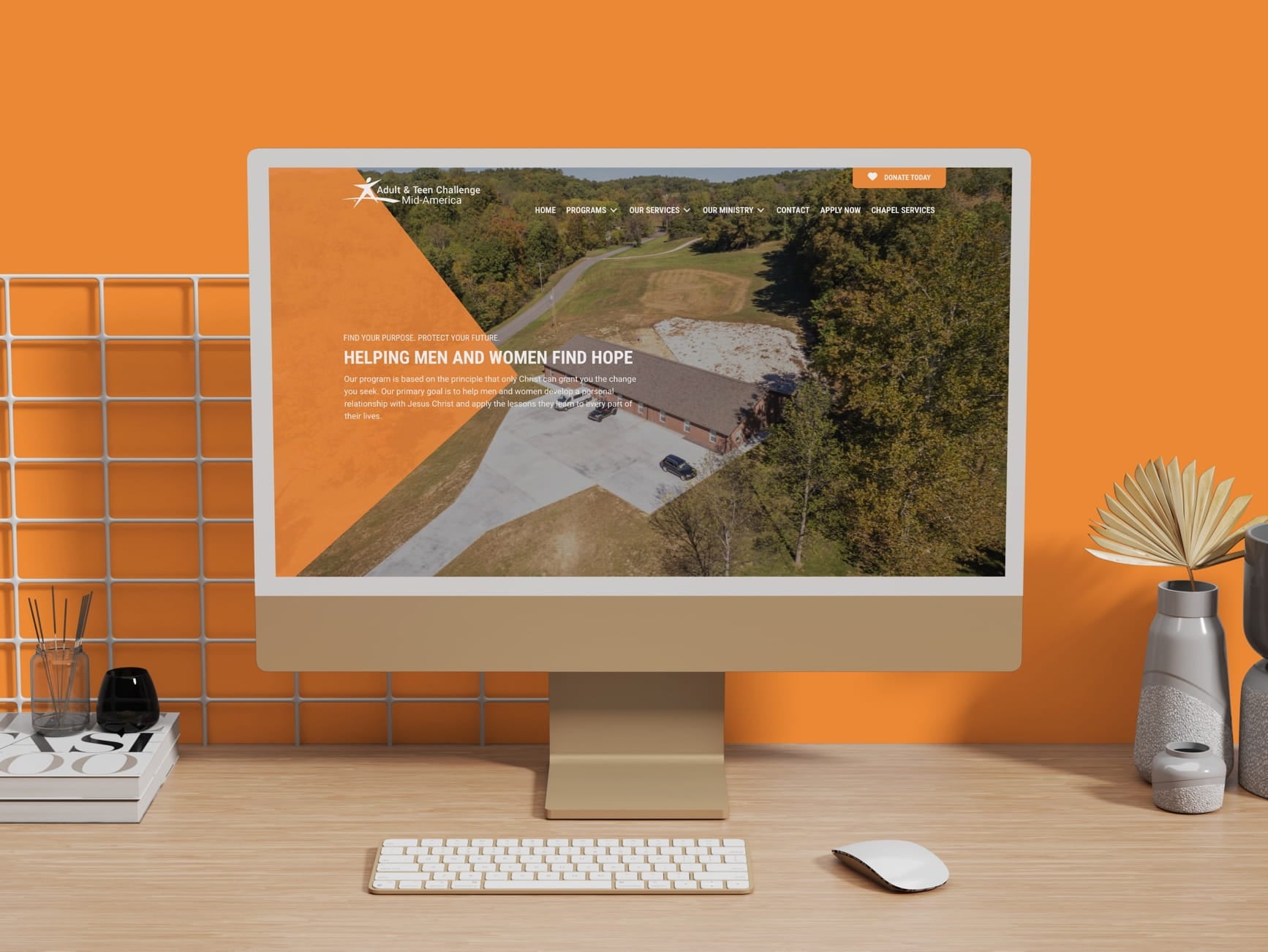 A monitor shows the Adult & Teen Challenge Mid-America website with orange header, navigation and a photo of a building.