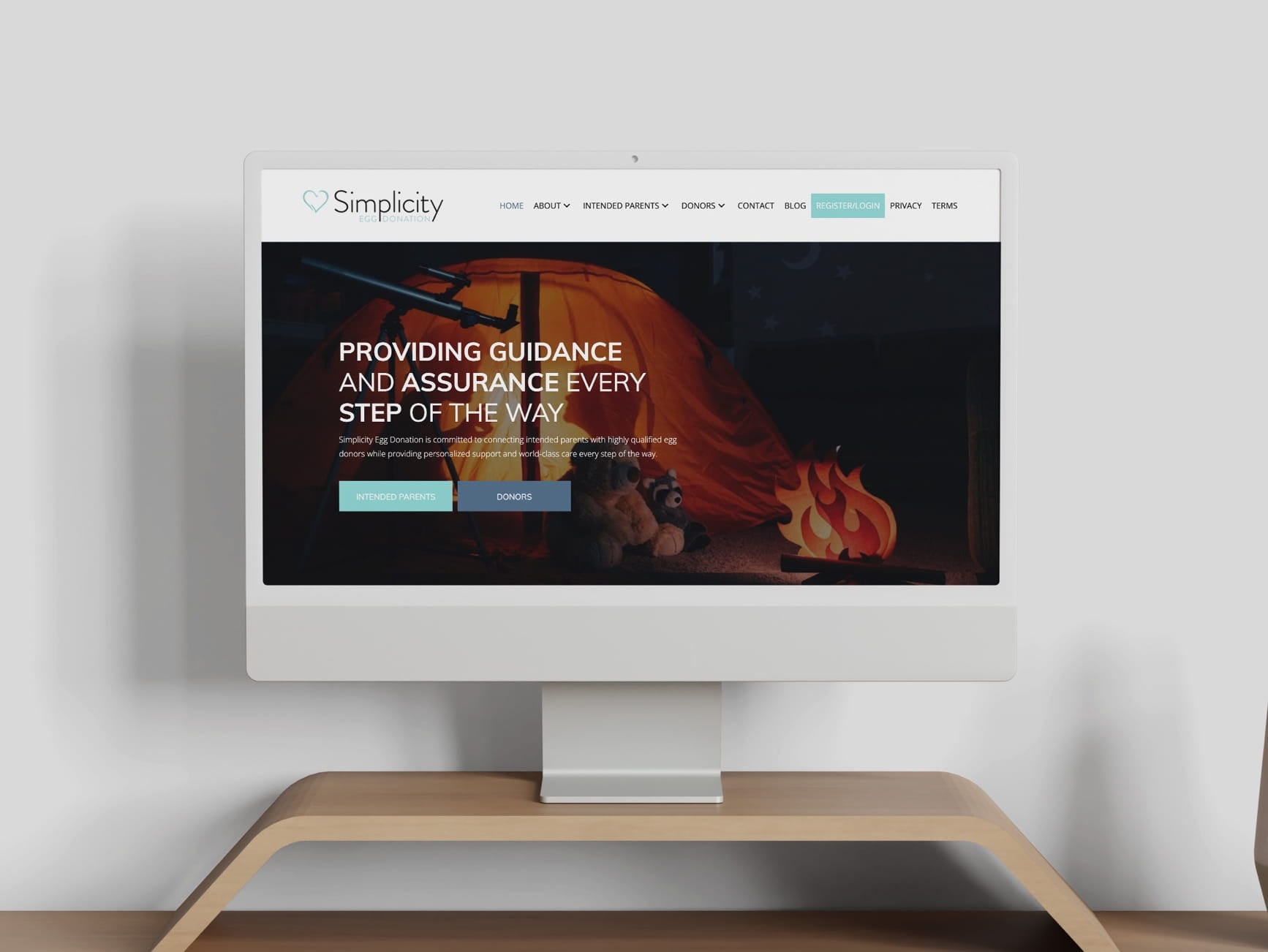 Monitor displays Simplicity Egg Donation site with image of tent, telescope, animals, fire, and parents/donors buttons.
