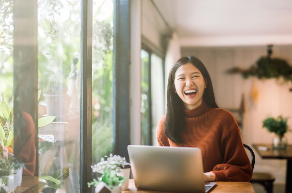 Happy young asian girl working at a coffee shop with a laptop