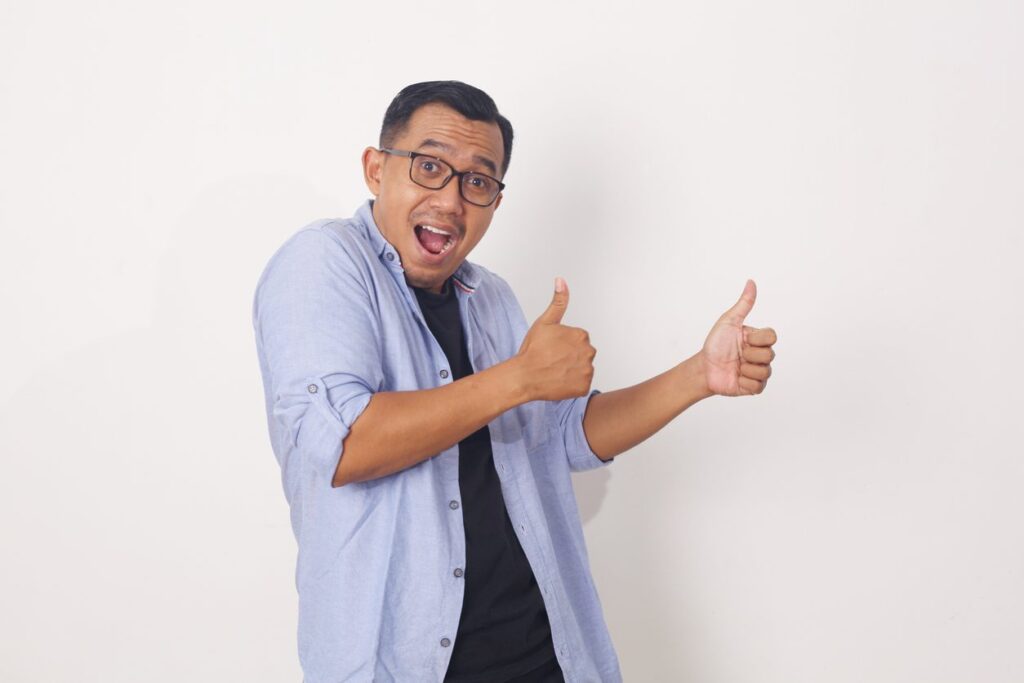 Expressive young handsome casual Asian man giving thumbs up. Isolated on white background