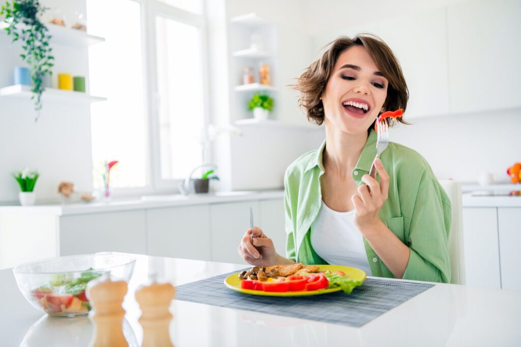 Portrait of funky excited girl sit chair kitchen table fork hold pepper enjoy homemade breakfast plate house indoors.