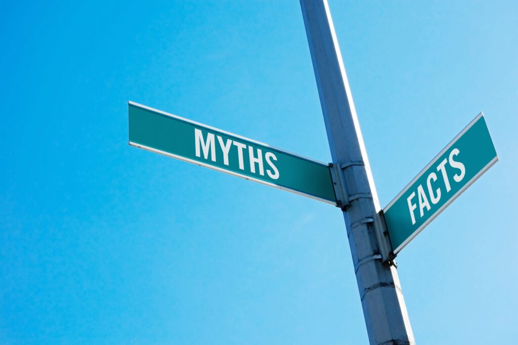 Green street signs labeled 'MYTHS' and 'FACTS' intersect on a pole against a clear blue sky.